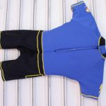 Kids' blue short-sleeve wetsuit with black leg panels, yellow trim, and front zipper, hanging on a white background.