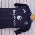 Dark blue Manchester United football jersey with geometric zigzag patterns, Adidas logo, club crest, and Snapdragon branding, displayed on a mannequin torso.