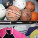 Sports Ball Collection featuring Boston Celtics basketball, Spalding basketball, Varsity soccer ball, and multicolor volleyball, displayed on a shelf with sports apparel beneath.