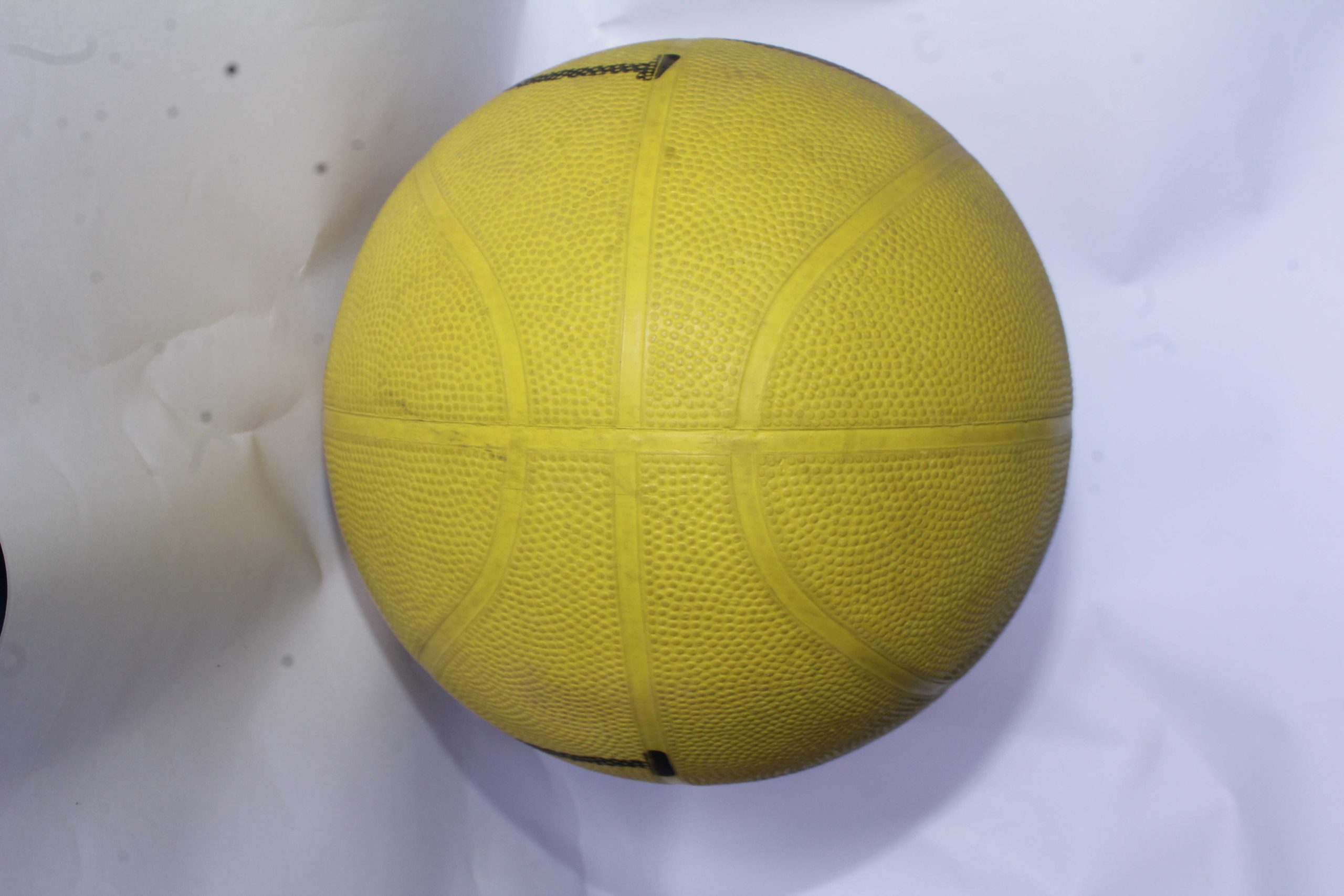Yellow basketball with textured surface and traditional panel lines, placed on a white background.