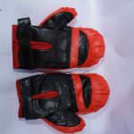Pair of black boxing gloves with red thumb padding, wrist straps, and knuckle protection, displayed on a white surface.
