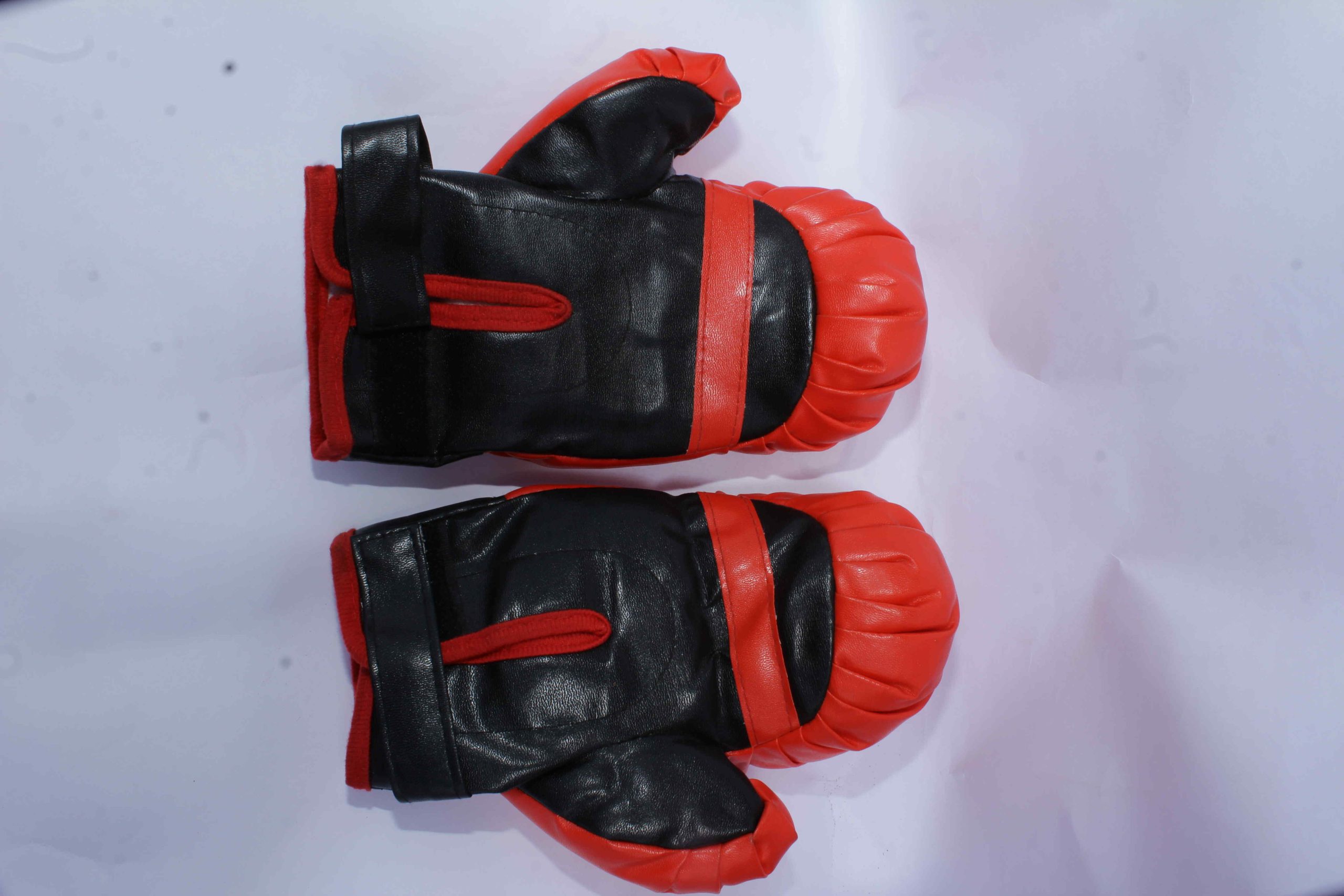 Pair of black boxing gloves with red thumb padding, wrist straps, and knuckle protection, displayed on a white surface.