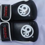 Black 9ROUND kickboxing gloves with white accents, featuring wrist straps with \"9ROUND 30 MIN KICKBOX FITNESS\" text and a circular logo on the main glove surface, displayed on a light-colored surface.