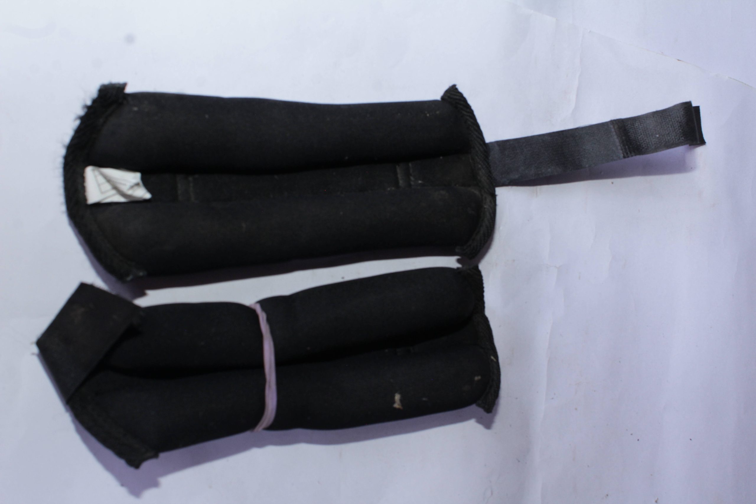 Black adjustable wrist and ankle weights with padded fabric and secure straps, placed on a white surface.