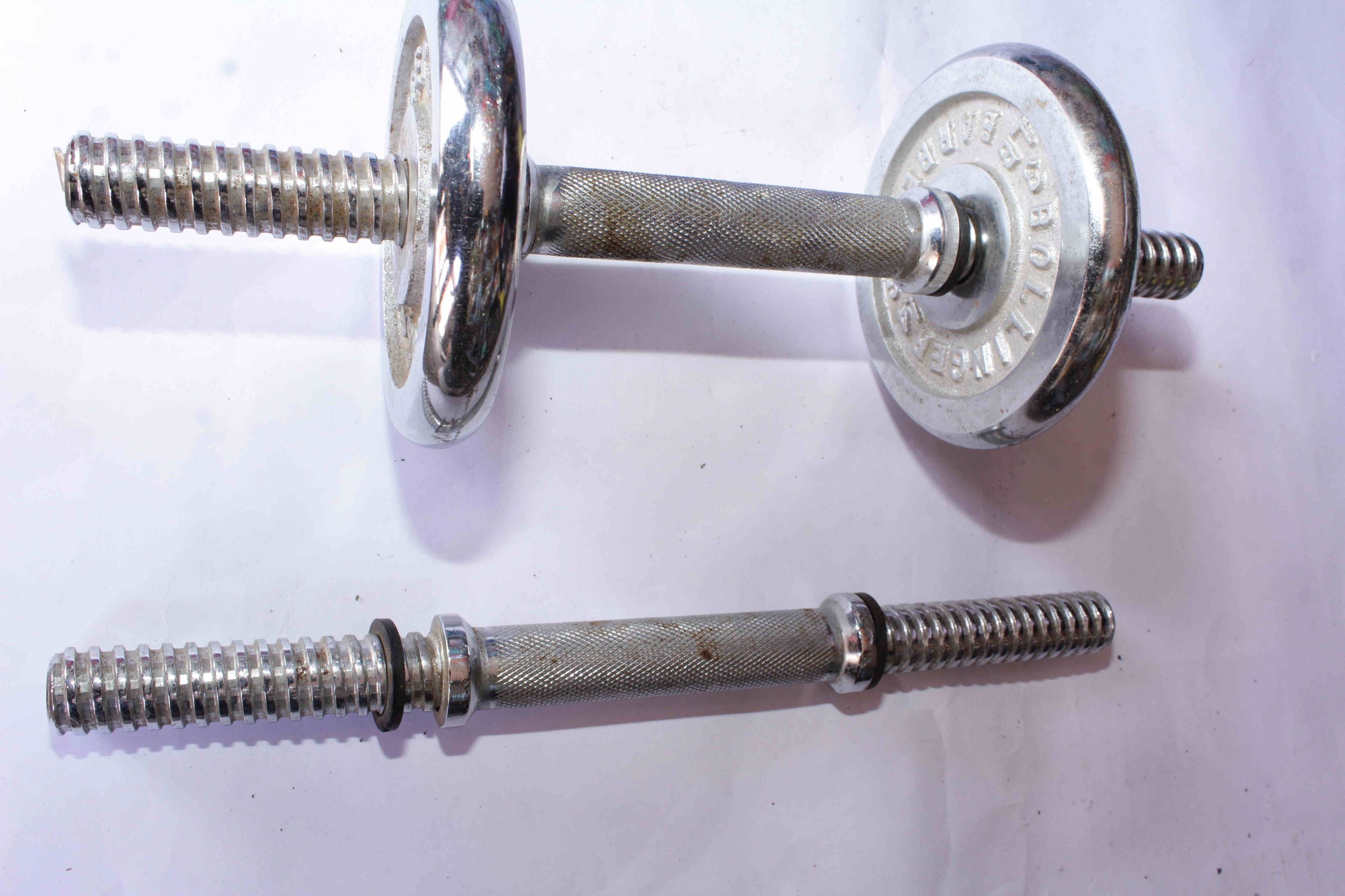 Two metal dumbbells—one fully assembled with weight plates, one without plates—featuring textured grips and threaded locking ends, displayed on a white surface.