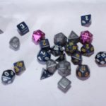 Collection of blue, gray, and pink polyhedral dice, including d4, d6, d8, d10, d12, and d20, displayed on a flat surface with visible numbers.