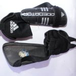 Black Adidas Predator Shin Guards with white Adidas branding, featuring a secure strap system for soccer protection.