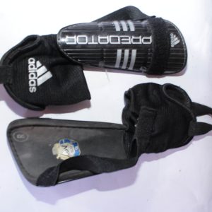 Black Adidas Predator Shin Guards with white Adidas branding, featuring a secure strap system for soccer protection.