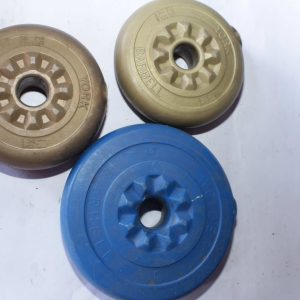 A close-up image of two cast iron weight plates placed on a white surface. One plate is beige with "York Barbell" branding, weighing 1.25 LB, while the other is blue with "Weider Barbell" branding, weighing 5 LB. The plates feature a circular design with raised text and grooves for easy grip.