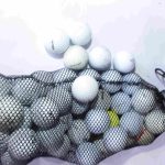 Assorted white and yellow golf balls with various brand markings inside and outside a black mesh bag, displayed on a light surface.
