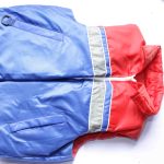 Sleeveless puffer jacket with red and blue color-block design, horizontal reflective stripes, front zipper, and side pockets, laid flat on a white surface.