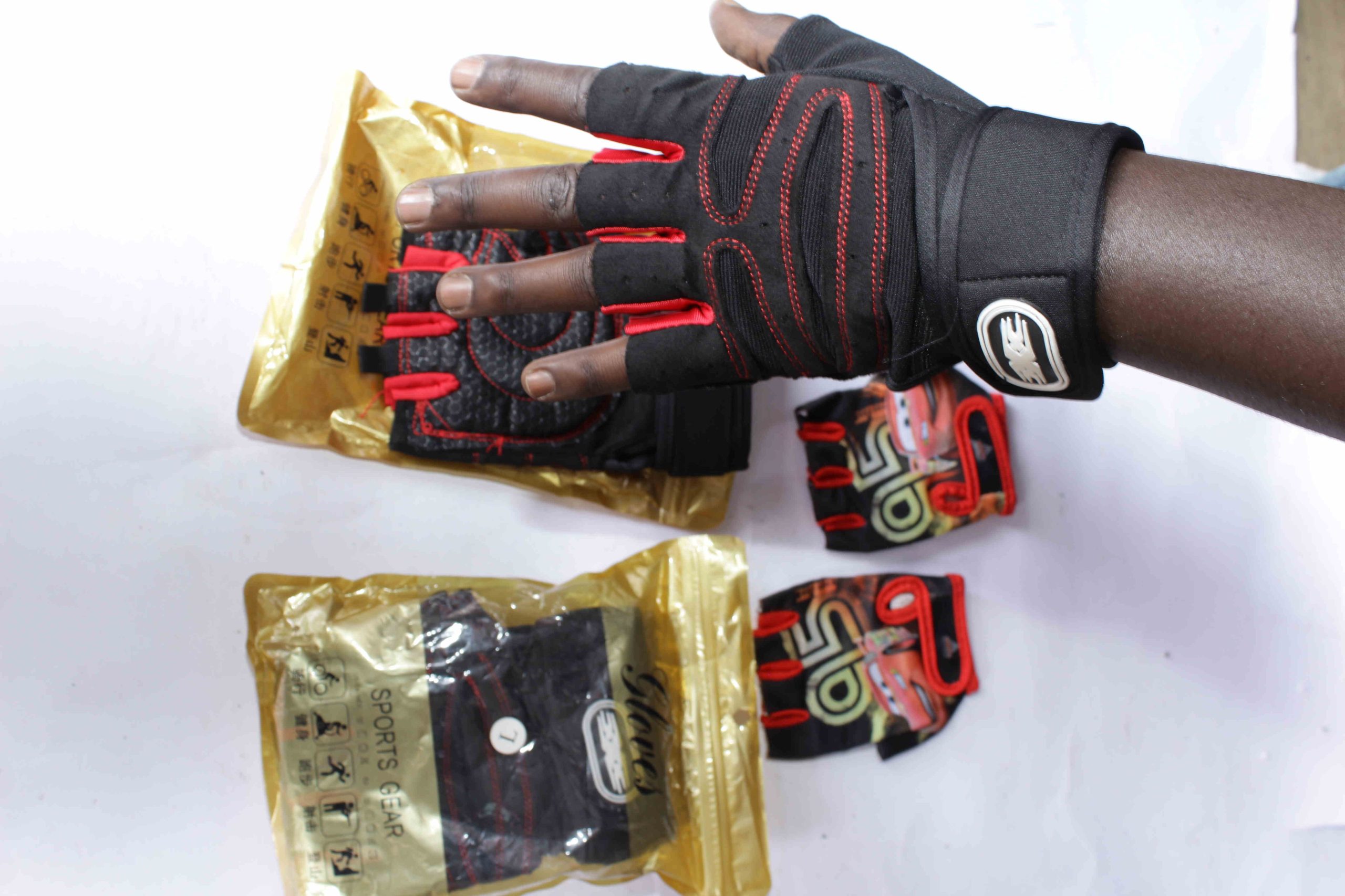 Sports & Cycling Gloves featuring fingerless designs, padded palms, and stylish black-red or themed Lightning McQueen models, displayed with gold packaging labeled "SPORTS GEAR".