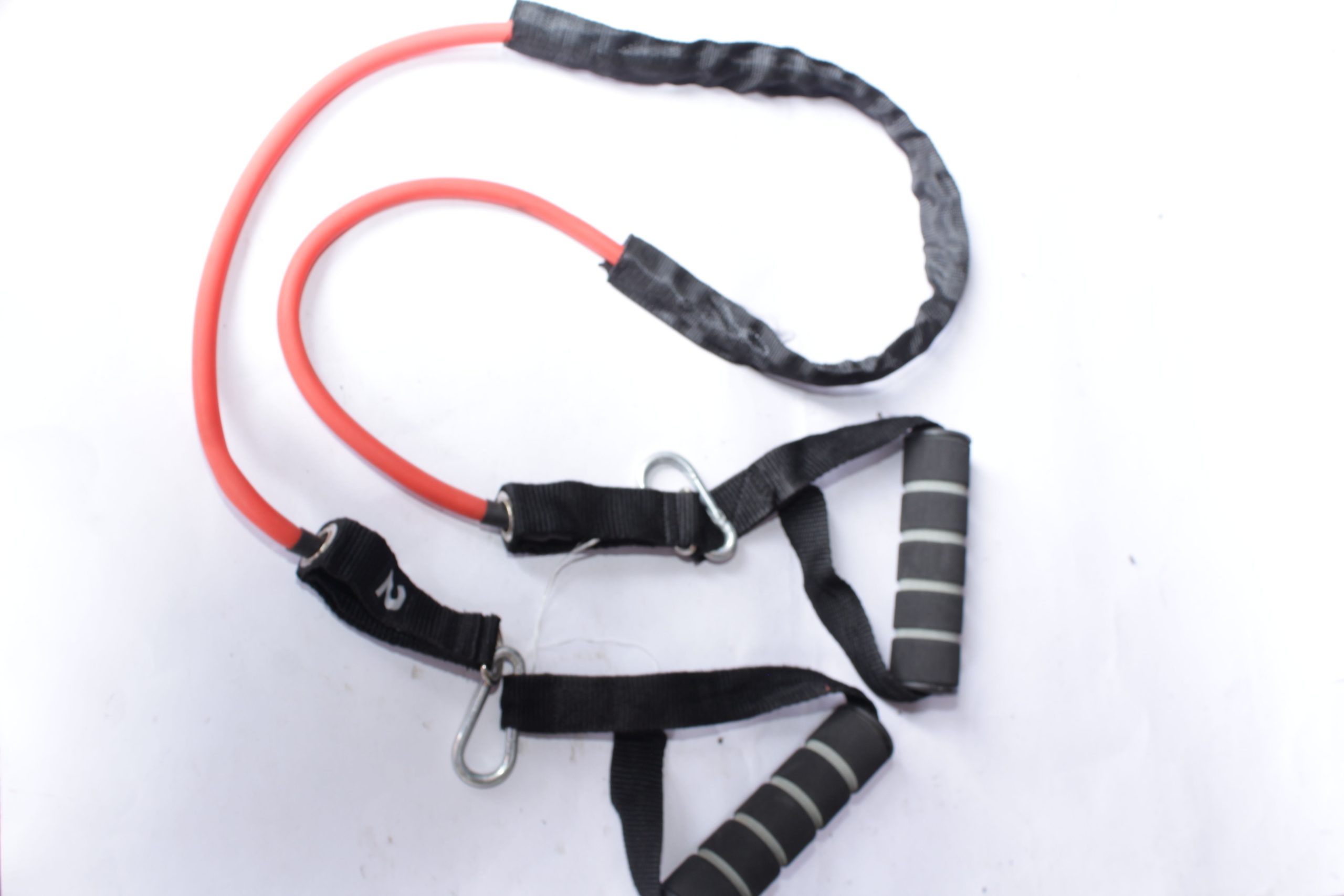 Red resistance band with black foam handles, secured by metal carabiners and sturdy black straps, displayed on a white surface.