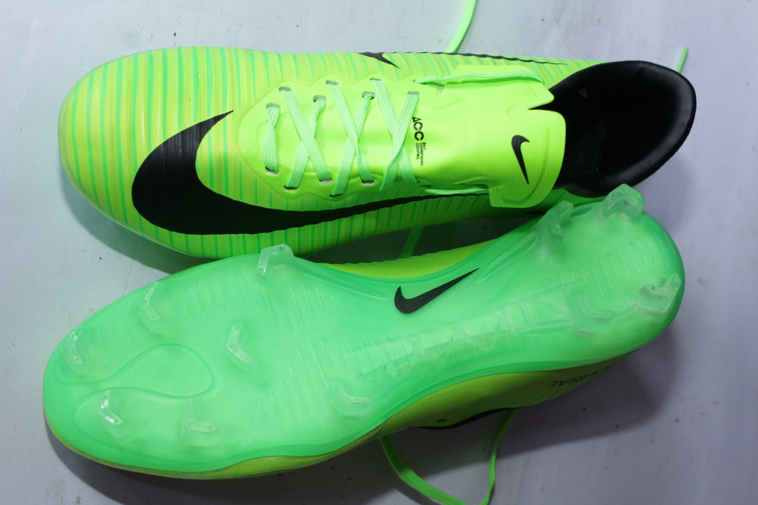 Bright green Nike ACC soccer cleats with black branding, textured grip, and translucent studded sole for firm-ground traction, displayed on a white surface.