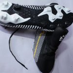 Black and white KM soccer cleats with a yellow zigzag design, white studded sole, and lace-up closure, displayed on a white background.