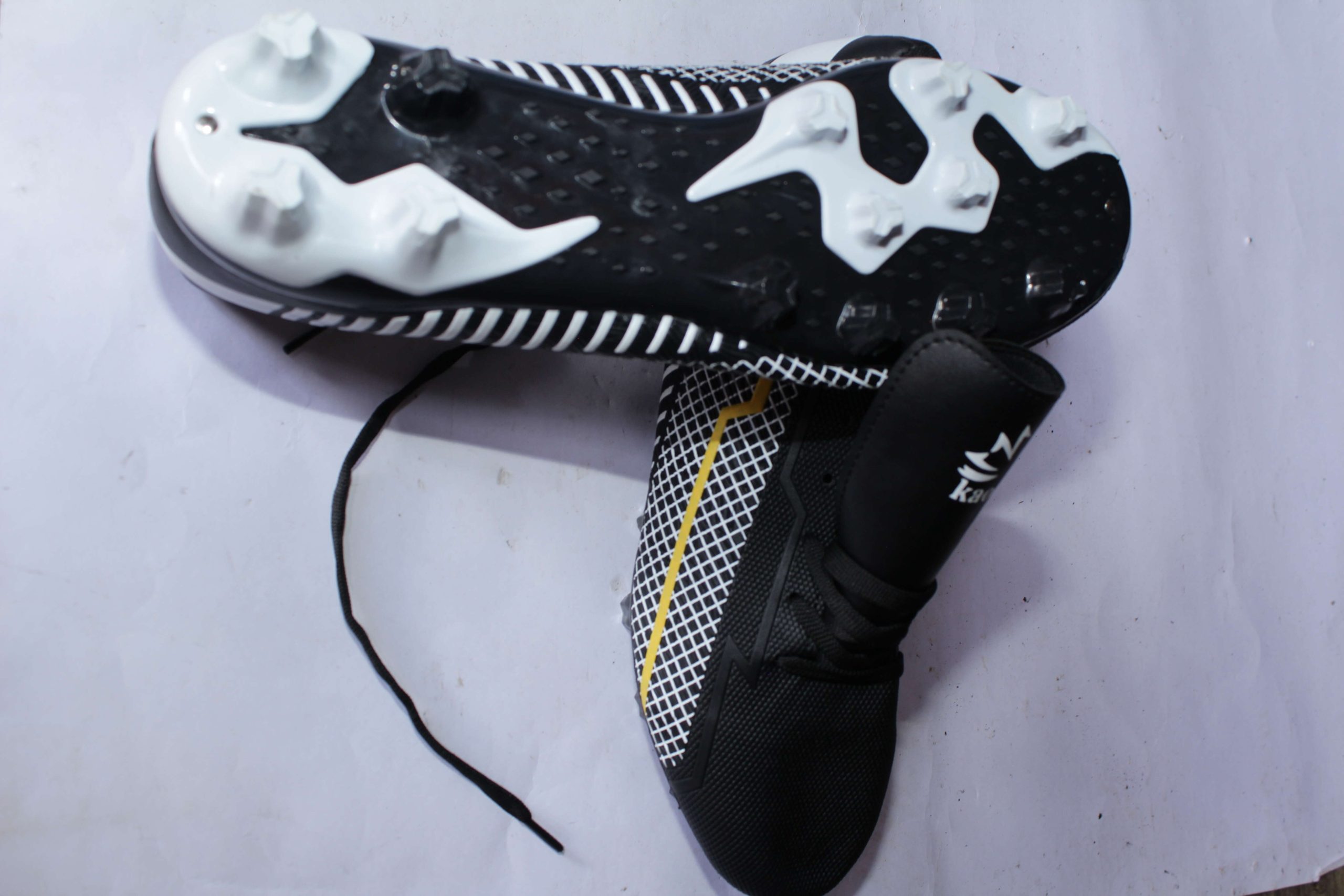 Black and white KM soccer cleats with a yellow zigzag design, white studded sole, and lace-up closure, displayed on a white background.