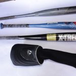 A set of four baseball bats laid out on a white surface, including Easton, Spider-Man, X-Treme, and a protective bat sleeve.